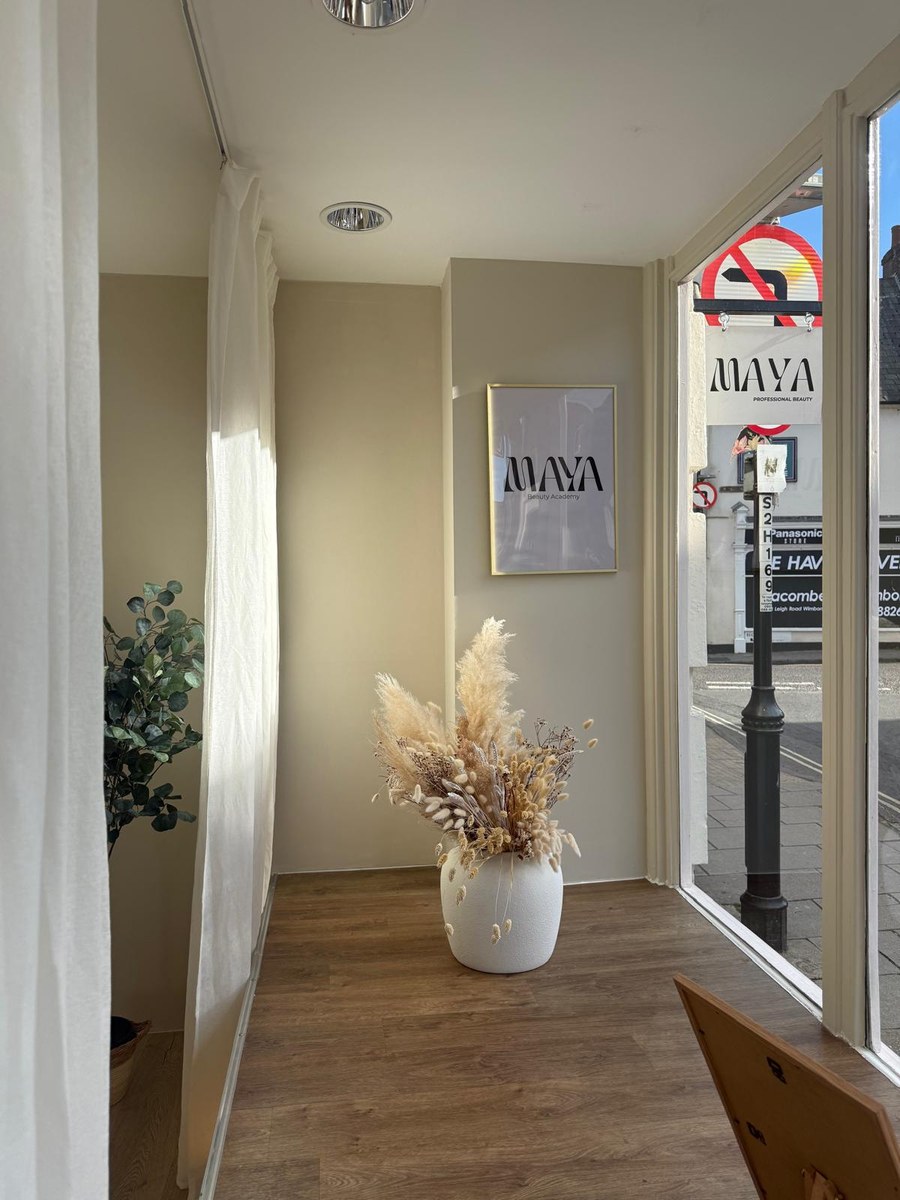 The Maya Beauty Academy poster on the wall of the salon, with a dried flower arrangement and the High Street outside