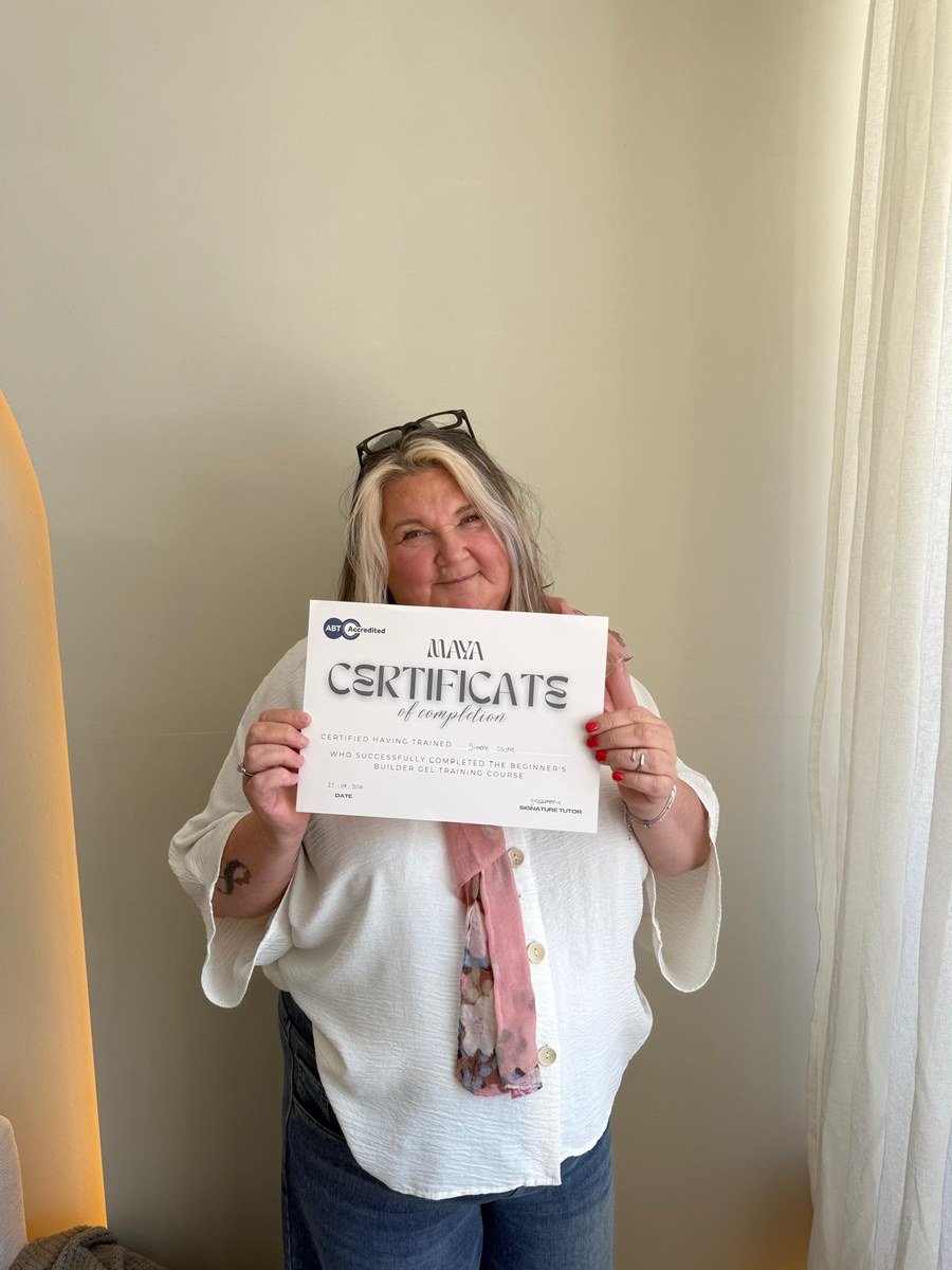 A Maya Academy graduate holding her certificate of completion for the Beginner's Builder Gel course