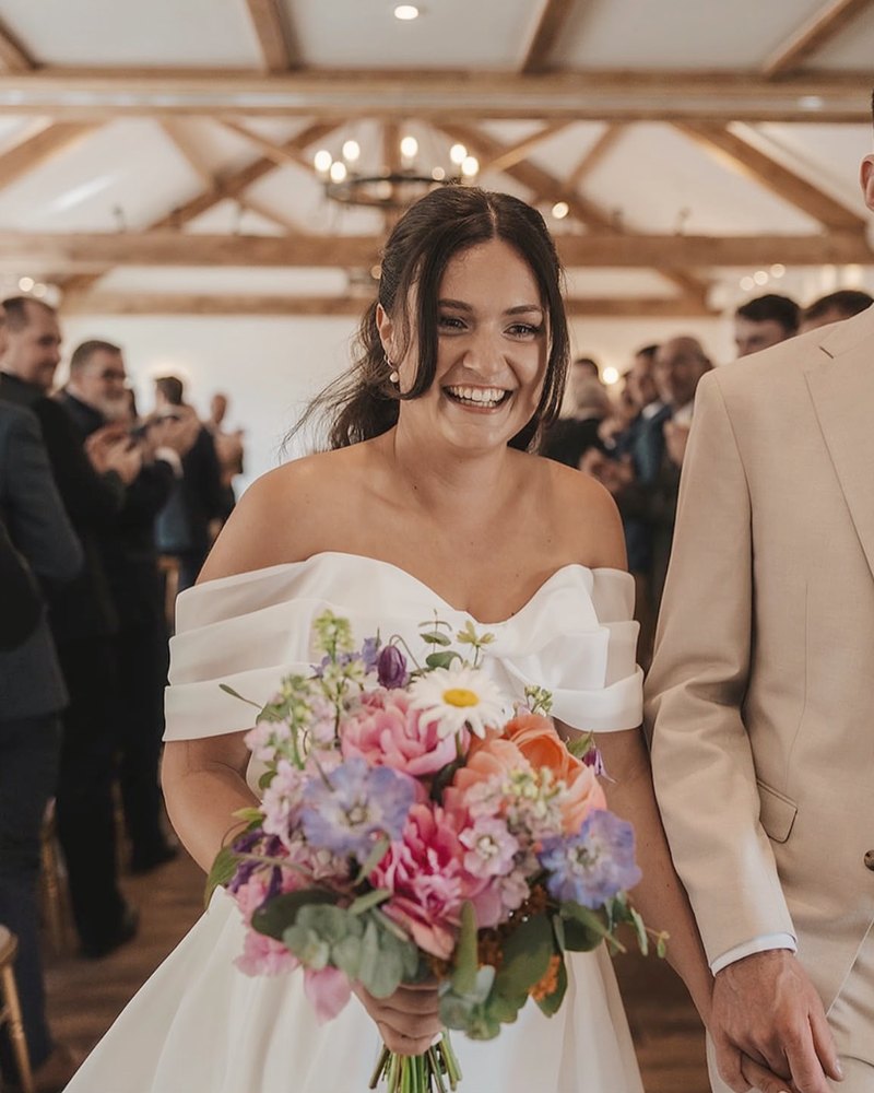 A bride smiling as she walks down the aisle with a bouquet