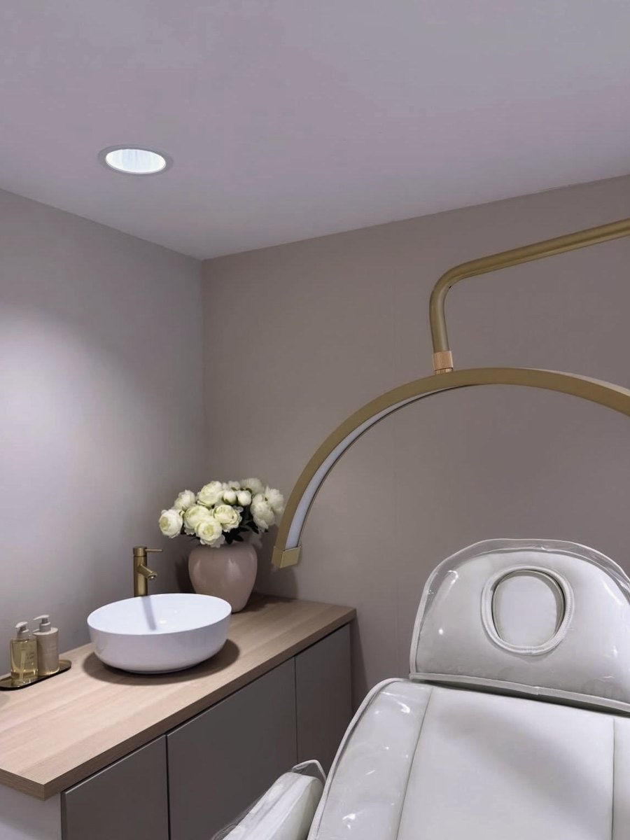 Maya treatment room with gold arched lamp, white treatment chair and basin with fresh flowers