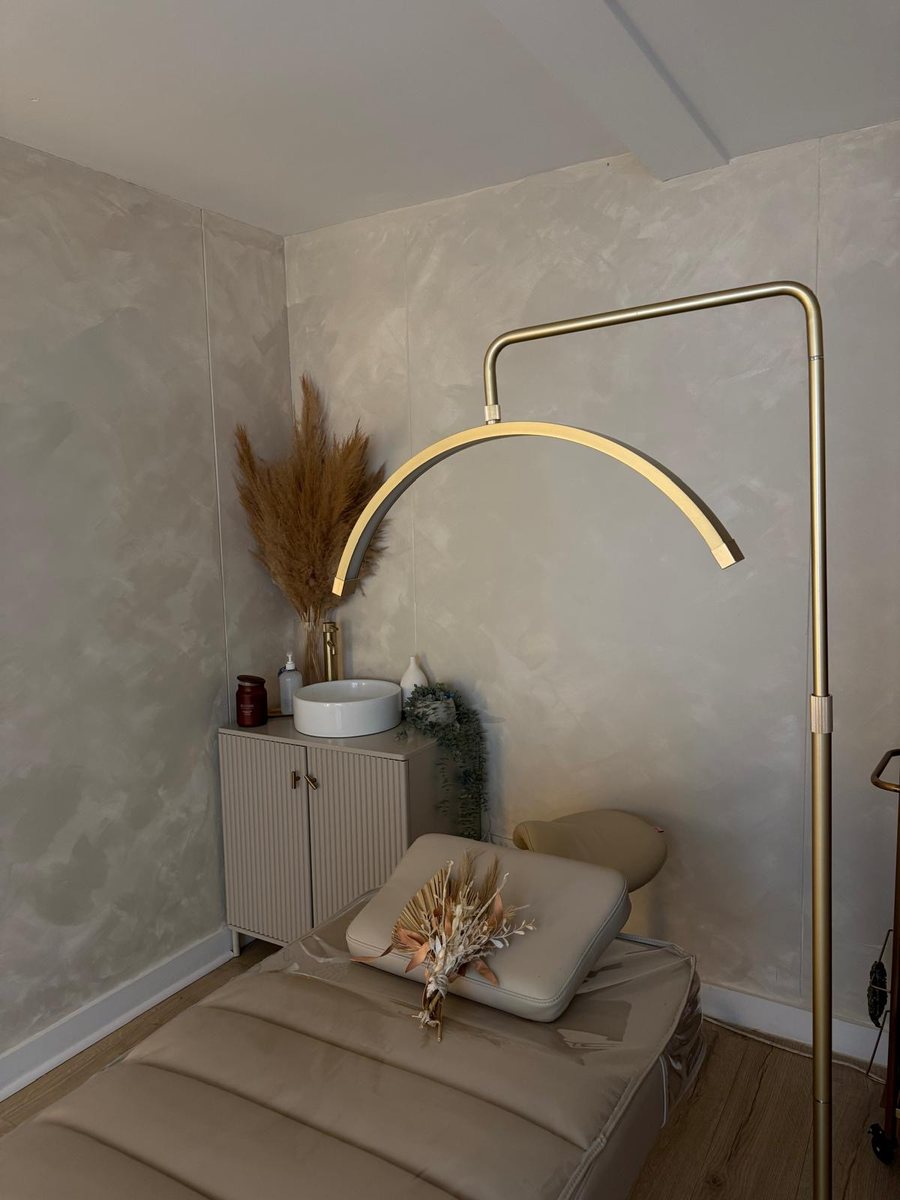 Maya treatment room with a gold arched lamp, cream treatment bed and dried pampas arrangement
