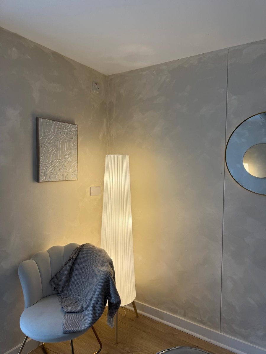 Quiet corner of the salon with a soft glowing lamp, shell armchair and textured plaster walls