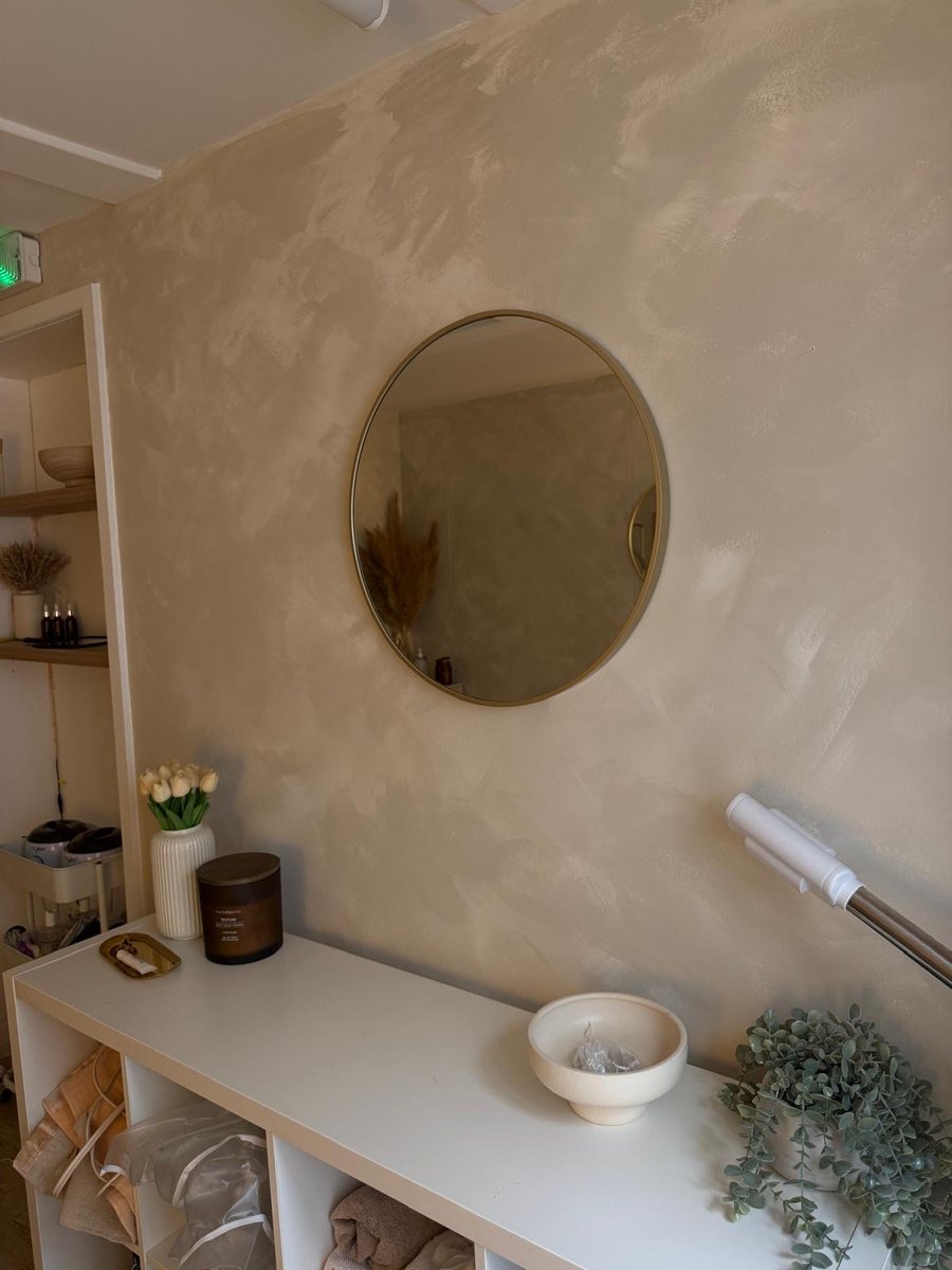 Maya treatment room with a round gold mirror, white shelving and neatly stacked towels